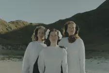 Tre kvinnor klädda i vitt står i en dal. Foto. 